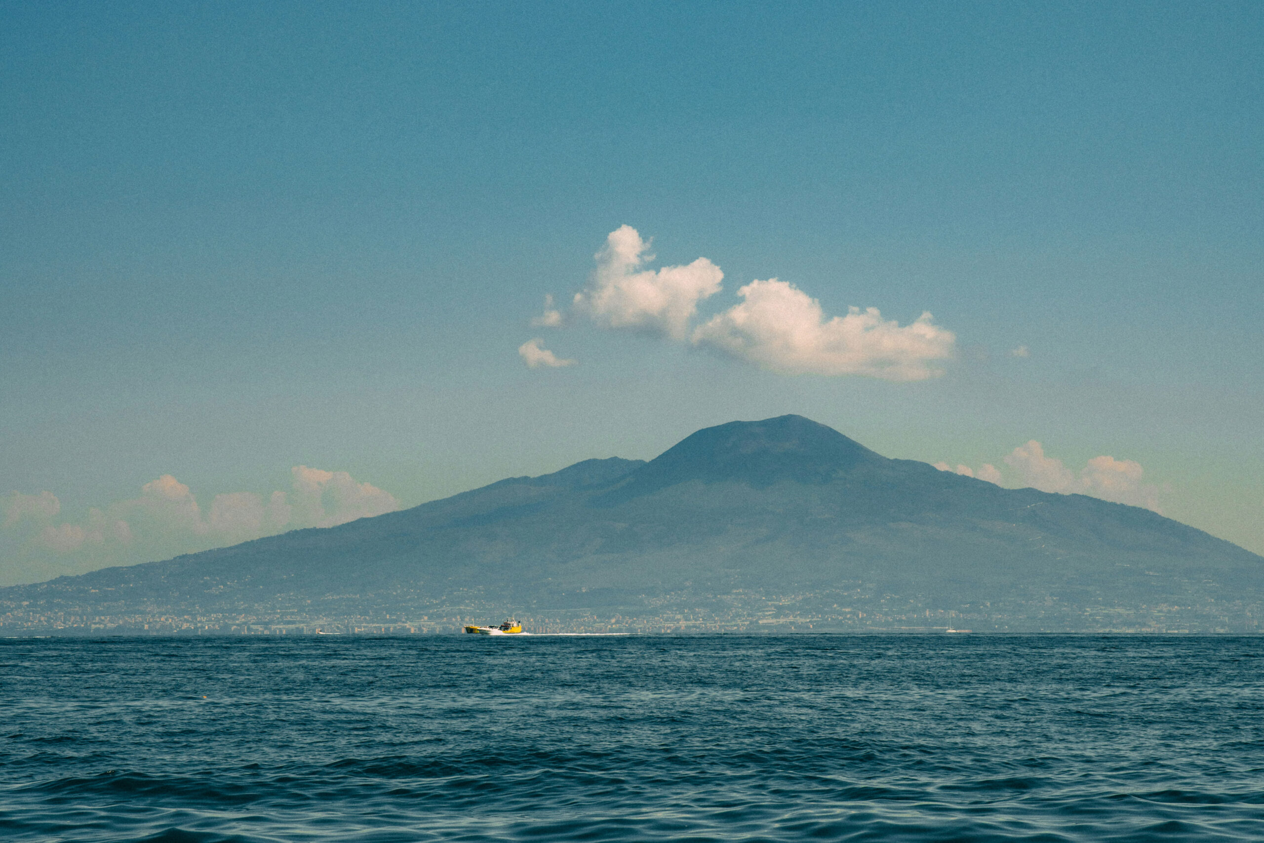 山を背景にした海を走る小さな黄色の船